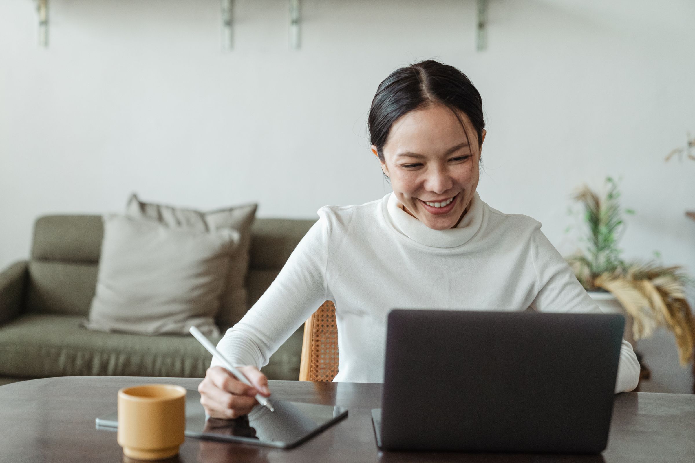 Smiling professional signing on a tablet beside her laptop.