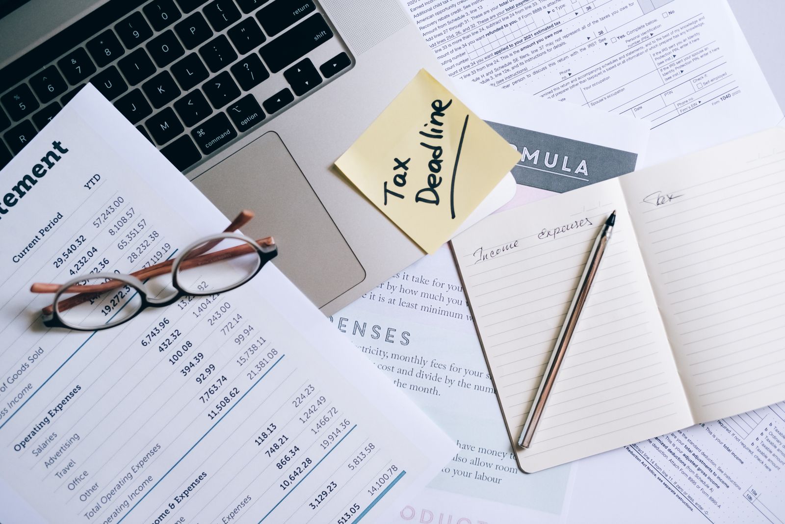 Tax documents and a financial statement beside a laptop.