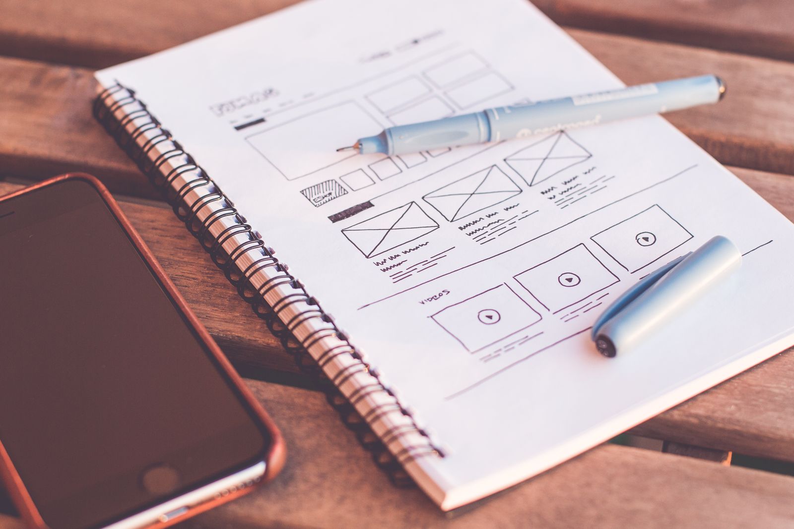 Screen design sketches in a notebook beside a phone.